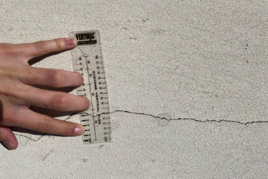 Personne mesurant une fissure au sol avec un mètre ruban.